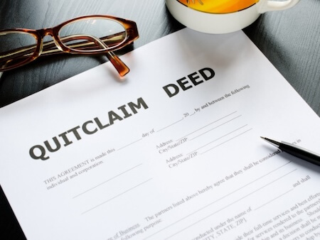 Deed Conveyance - Quitclaim deed on top of a table, with it is a pair of glasses and a pen.
